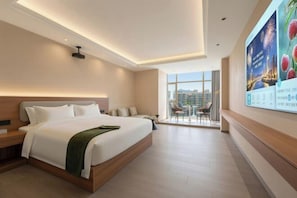 Een moderne hotelkamer met een groot bed, een bureau, een stoel en een balkon met uitzicht over de stad.