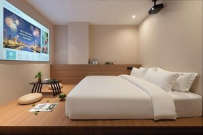 Ein modernes Hotelzimmer mit einem großen Bett, einem kleinen Tisch mit einer Pflanze, einem an der Wand befestigten Fernseher und einer Holzplattform mit einer Zeitschrift und einem Kissen.