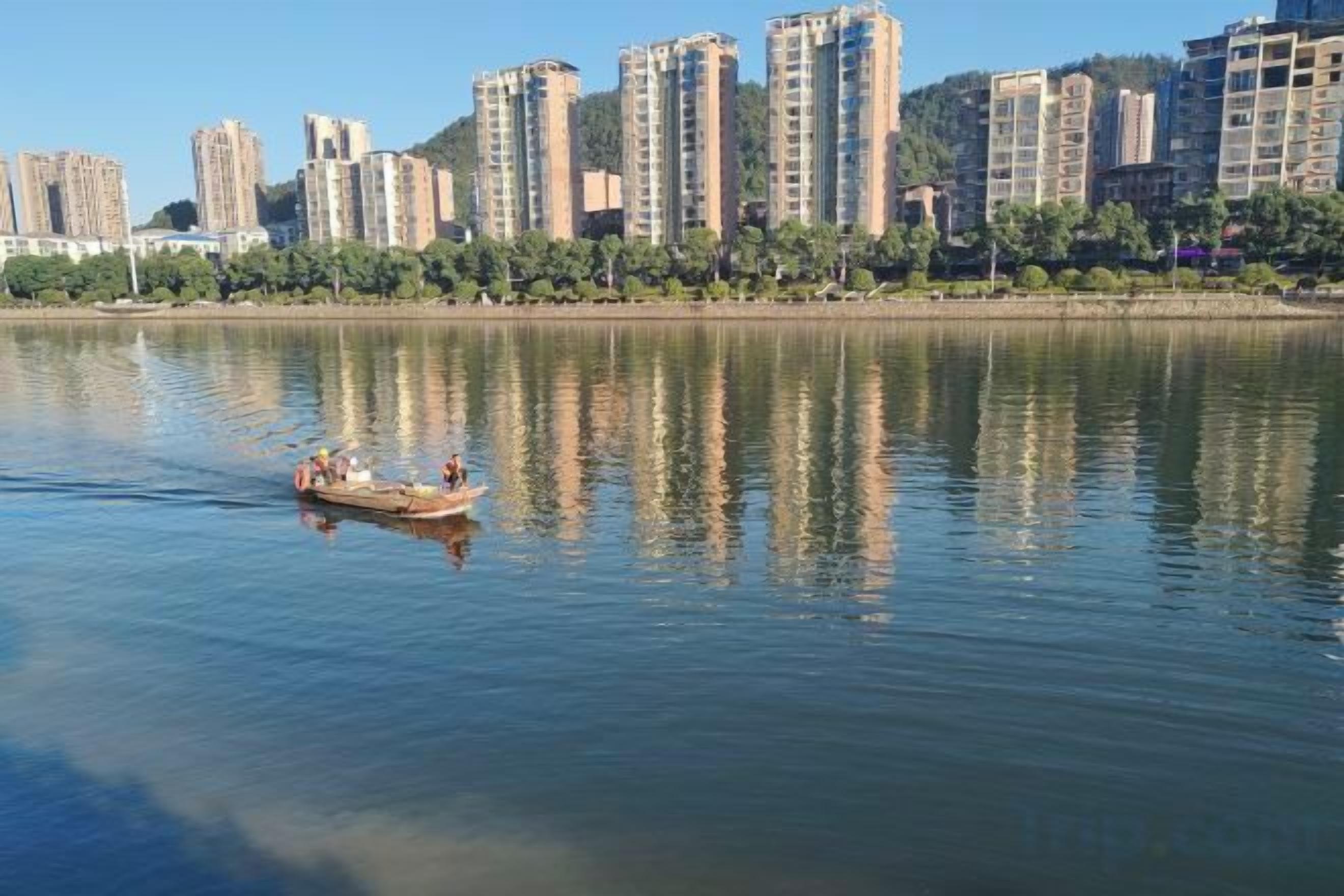 A calm river with a boat carrying people, surrounded by high-rise buildings.