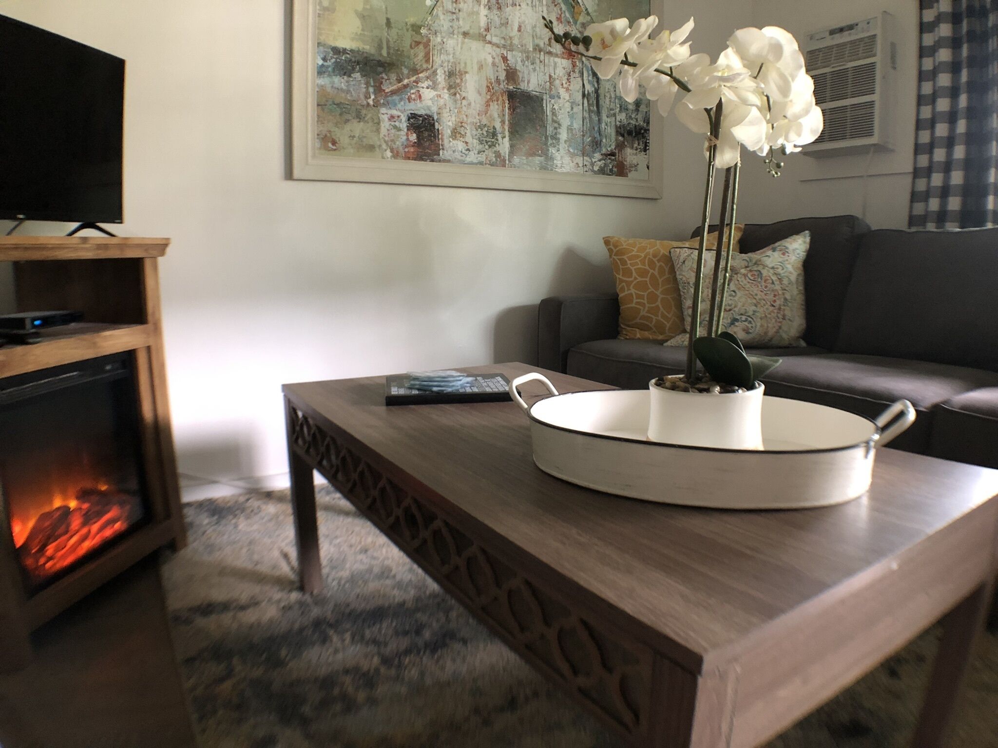 Un salon avec une cheminée, un canapé, une table basse ornée d’une plante et un tableau accroché au mur.