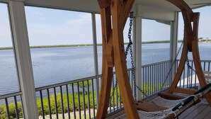 Una silla mecedora de madera en una terraza de madera, con vista a un lago tranquilo y follaje.