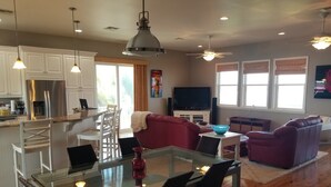Una cocina moderna con una isla central, comedor con mesa de vidrio y una sala de estar con sofá rojo.