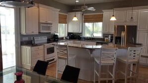 Una cocina moderna con armarios blancos, una isla central con taburetes y un refrigerador grande, además de un ventilador de techo.