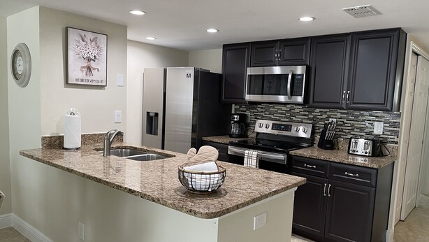 A modern kitchen with dark cabinetry, stainless steel appliances, and a granite countertop. - LOVELY LUXURY APARTMENT CLOSE DISNEY (Kissimmee)