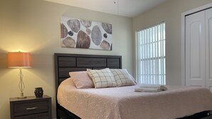 A bedroom with a bed, a nightstand, a lamp, and a window with blinds. - LOVELY LUXURY APARTMENT CLOSE DISNEY (Kissimmee)
