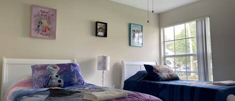 A bedroom with two beds, a ceiling fan, and a window with a view of the outside.