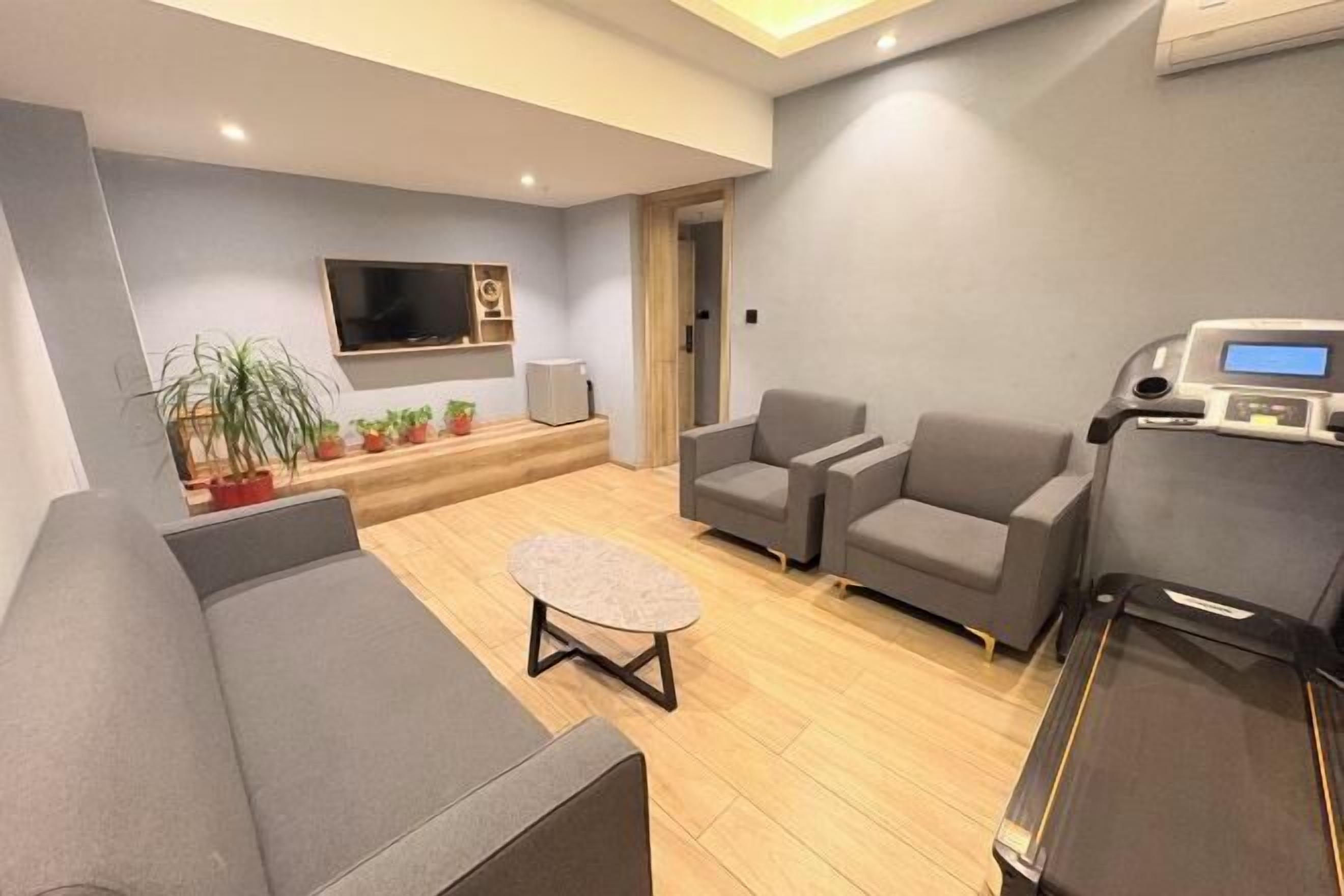 Uma sala de estar moderna com sofá, duas poltronas, mesa de centro, esteira, televisão de tela plana e um pequeno arranjo de plantas.