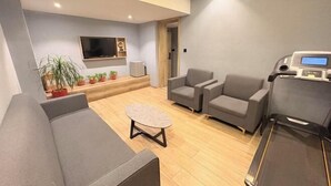 A modern living room with a sofa, two armchairs, a coffee table, a treadmill, a flat-screen TV, and a small plant arrangement. - Yahao Selected Hotel (Jinfeng Branch) (Zhangjiagang)