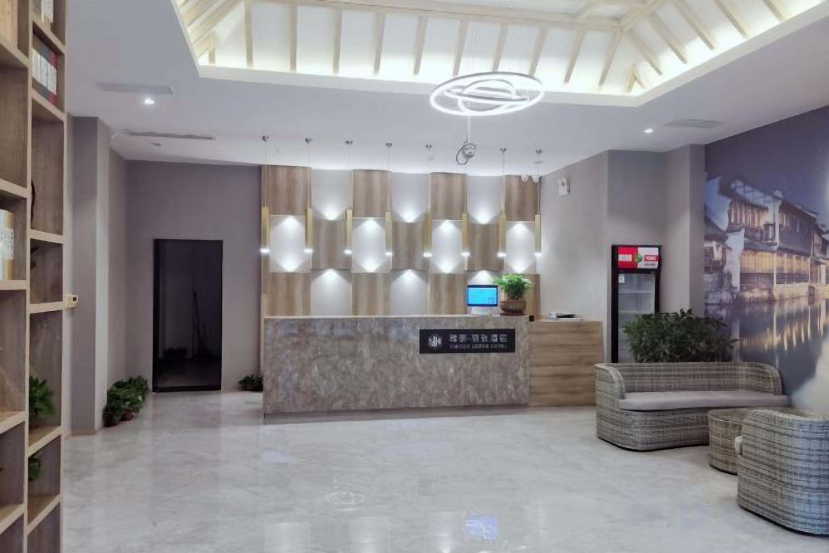 Een hotel receptie met een marmeren balie, hanglampen, een digitaal scherm en een zithoek met rieten meubels.