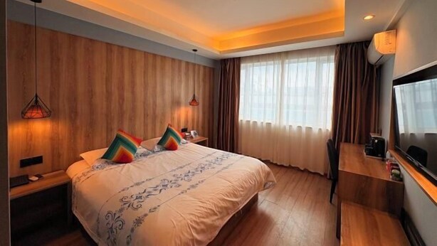 Une chambre d’hôtel moderne avec un grand lit, des murs lambrissés en bois, un bureau et une télévision.