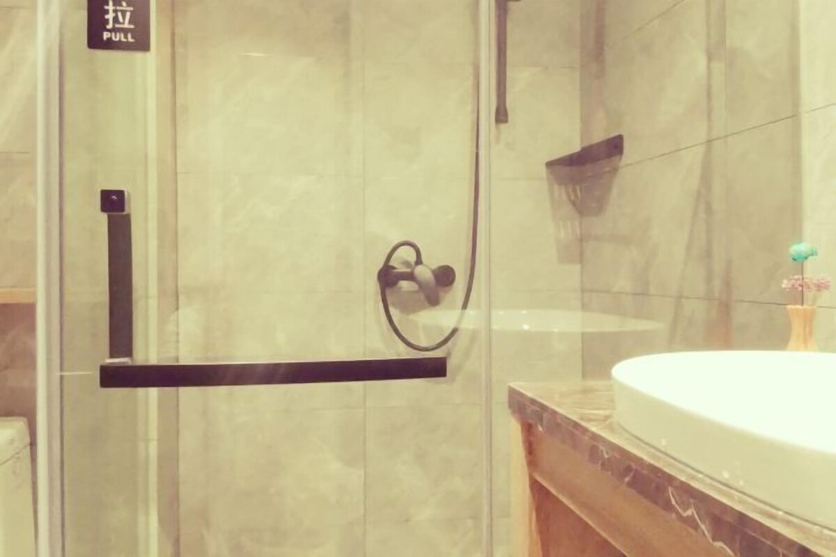 Casa de banho com divisória de chuveiro de vidro, lavatório com bancada de mármore e porta-toalhas.