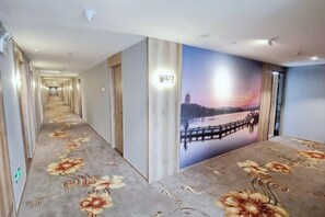 A hotel hallway with a long corridor, a mural of a sunset over a body of water, and a carpet with floral patterns. - Yahao Selected Hotel (Jinfeng Branch) (Zhangjiagang)