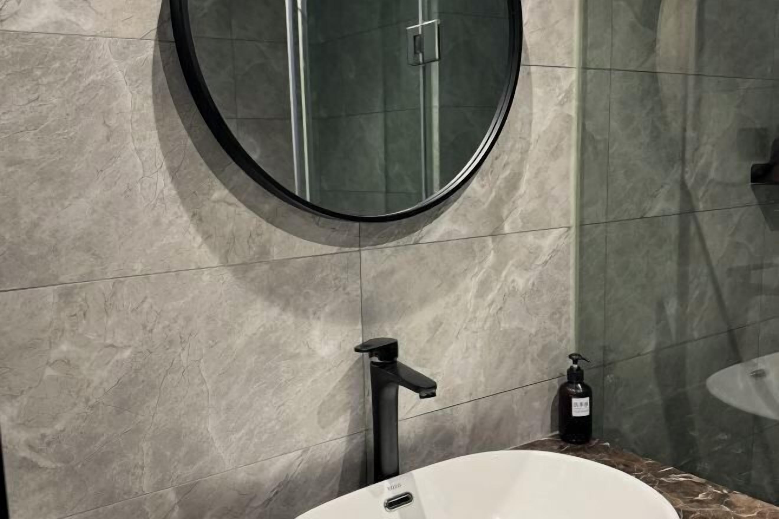 Un baño con un espejo redondo, un grifo negro y un lavamanos blanco.