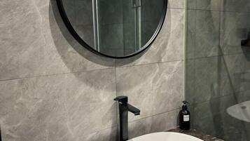 Un baño con un espejo redondo, un grifo negro y un lavamanos blanco.