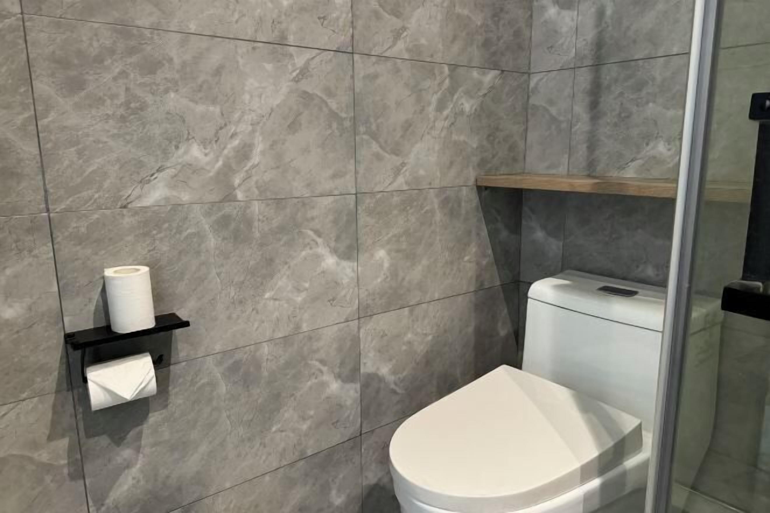 Een moderne badkamer met een toilet, een handdoekdispenser en een plank met een rol toiletpapier.