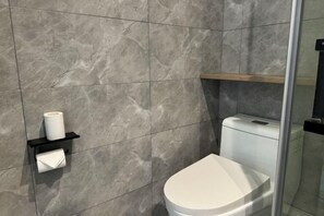 A modern bathroom with a toilet, a towel dispenser, and a shelf with a roll of toilet paper. - Yahao Selected Hotel (Jinfeng Branch) (Zhangjiagang)