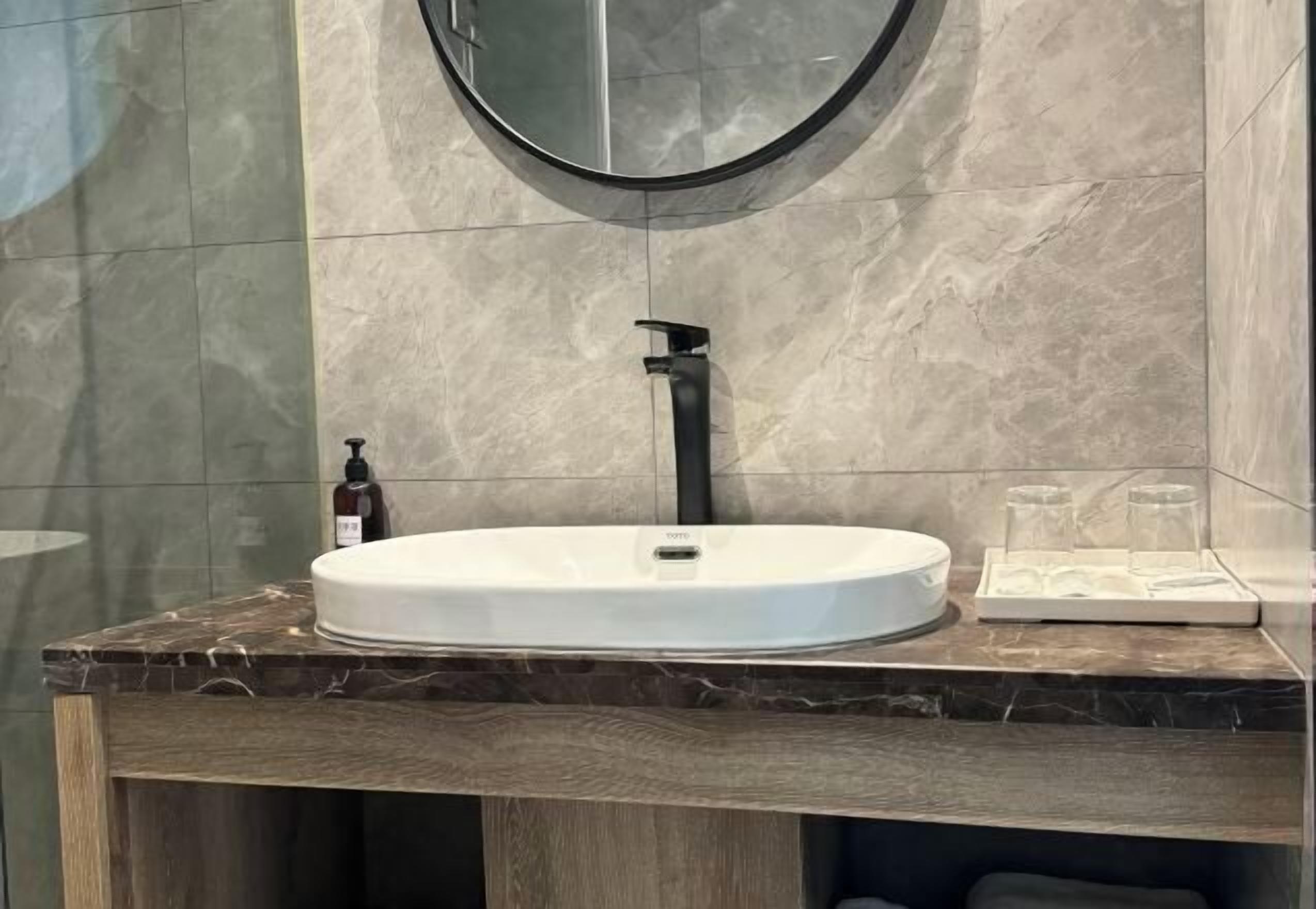 Un baño con un espejo redondo, un lavamanos blanco y una encimera de mármol.