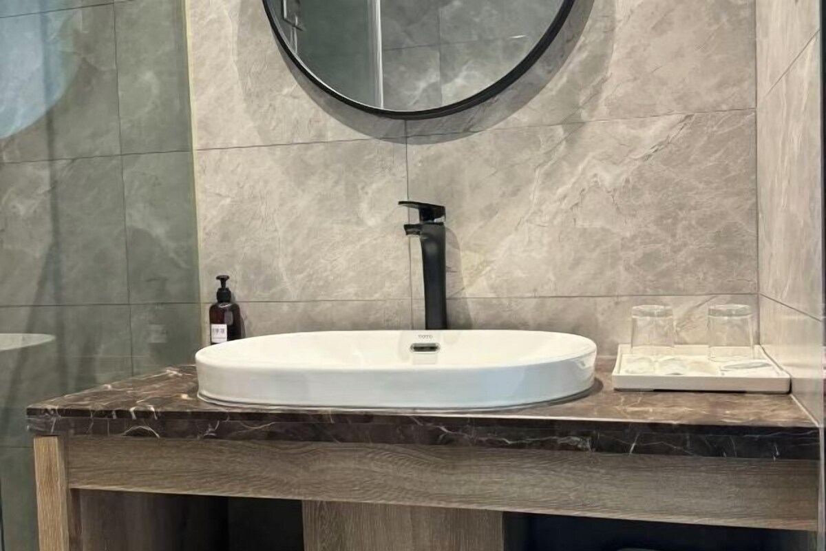 A bathroom with a round mirror, a white sink, and a marble countertop.