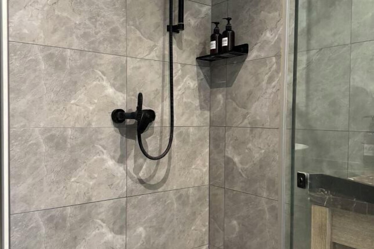 A shower area with a handheld showerhead and a wall-mounted control panel.