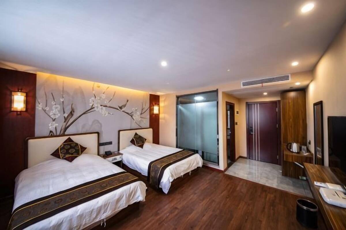 Une chambre d’hôtel avec deux lits, un plancher en bois, un climatiseur fixé au mur, un bureau avec une chaise et un téléviseur.