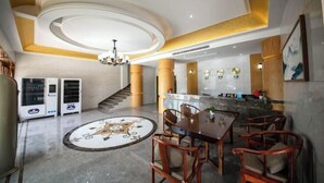 Un'ampia hall con pavimento in marmo, un'area salotto centrale con sedute in legno, un lampadario e una reception.