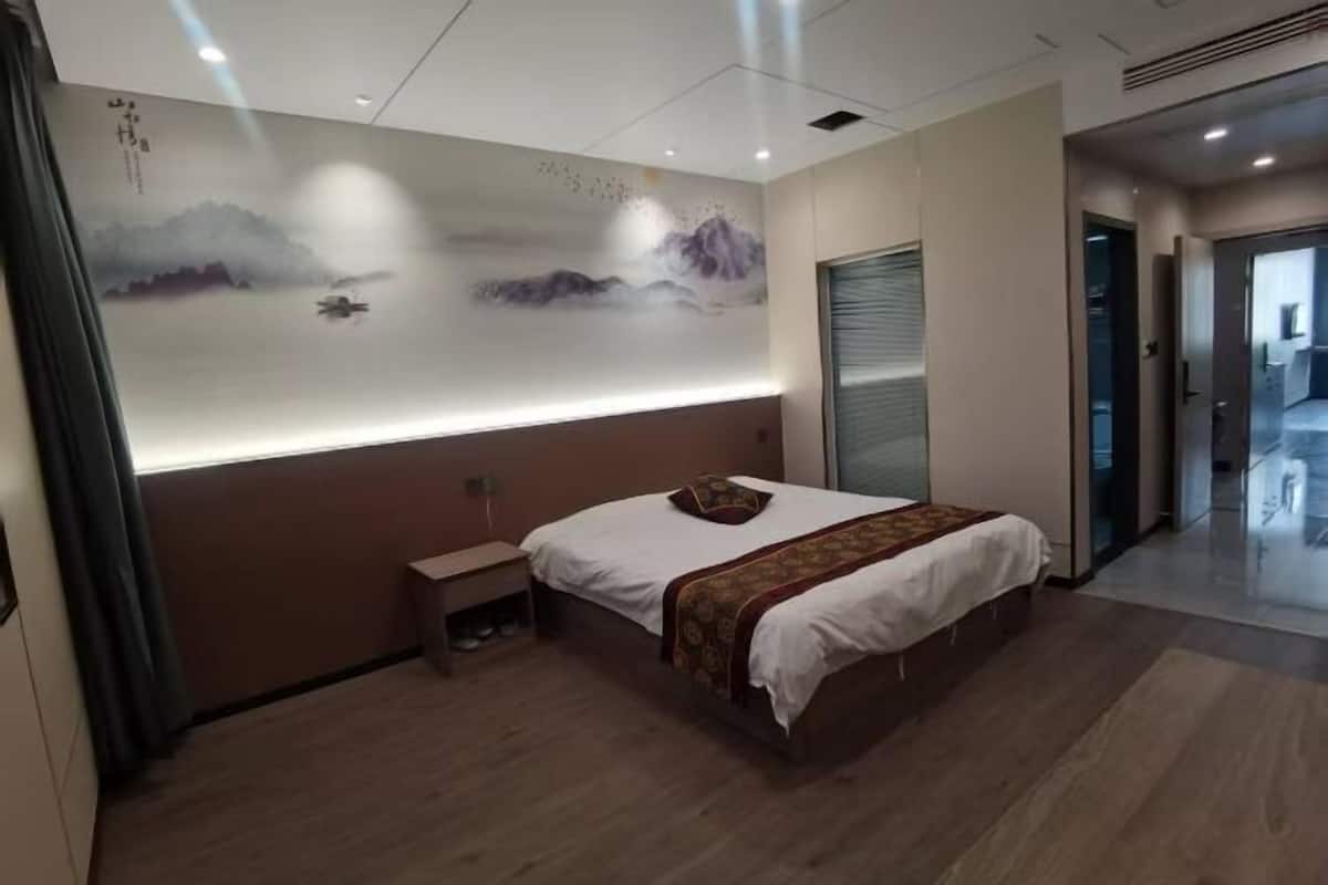 Une chambre d’hôtel moderne, dotée d’un grand lit, d’une petite table de chevet, d’une œuvre d’art accrochée au mur et d’une porte coulissante donnant sur une autre pièce.