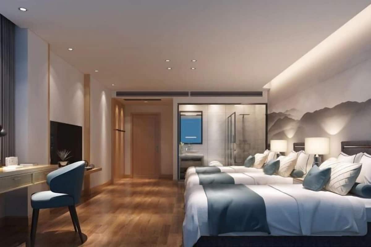 Une chambre d’hôtel moderne équipée d’un bureau, de deux lits, d’une télévision et d’une salle de bain avec douche.