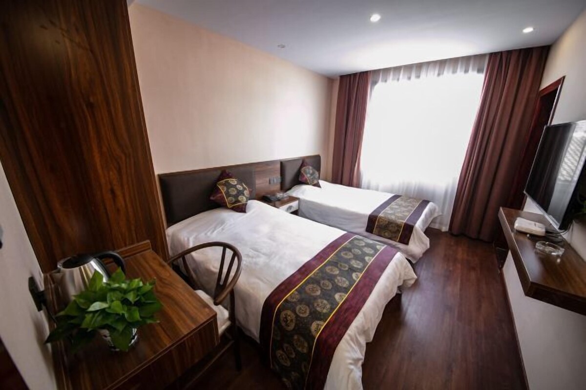 A hotel room with two beds, wooden furniture, a TV, and a plant.