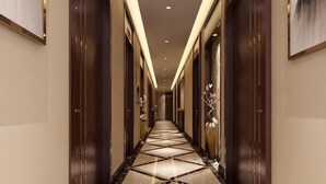 Un corridoio d'albergo con pavimento lucido, porte in legno scuro e illuminazione a incasso.