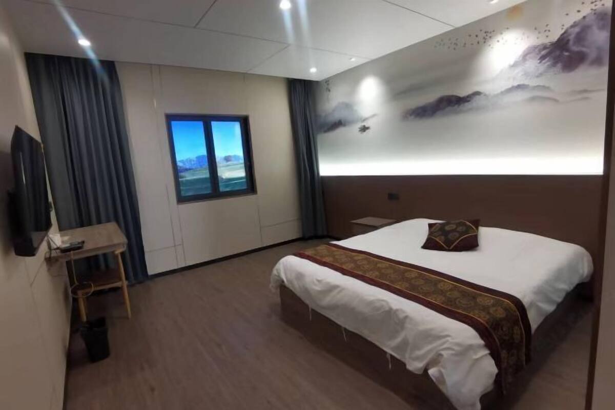 Une chambre d’hôtel avec un lit, un bureau, une télévision, une fenêtre donnant sur un beau paysage et une fresque murale.