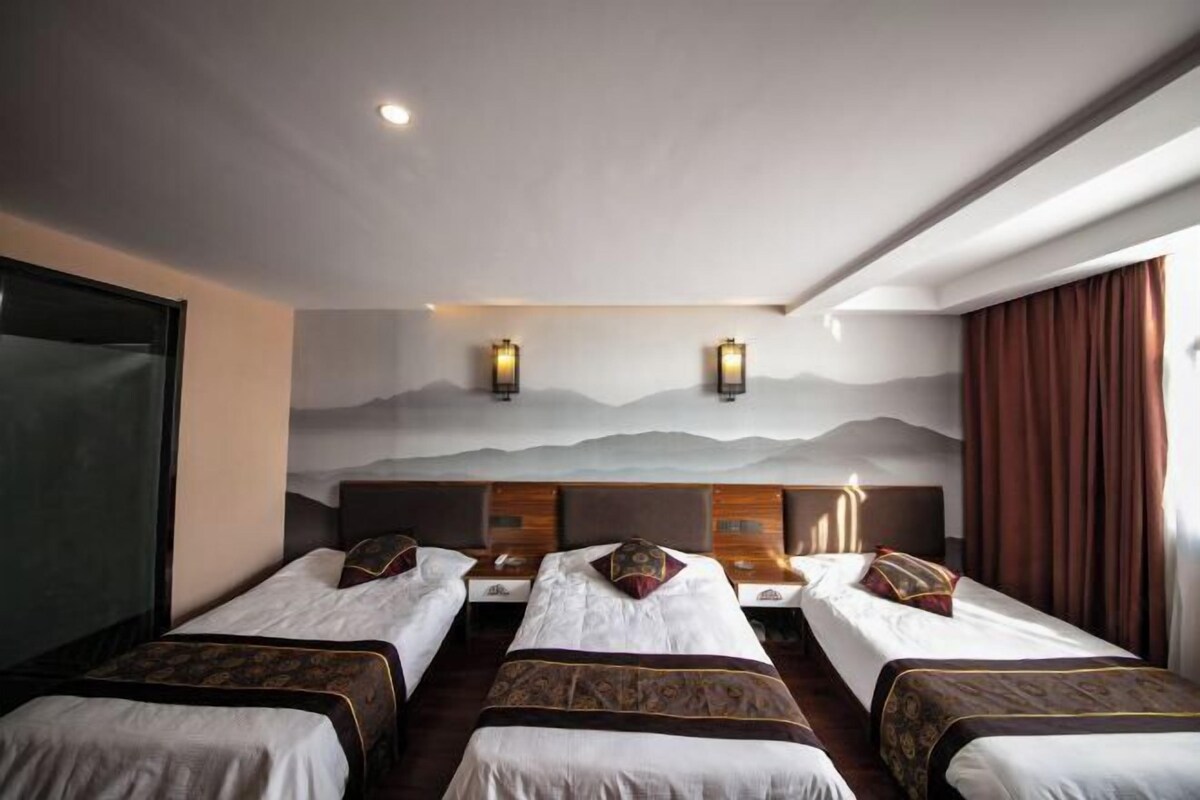 A hotel room with three beds, a large wall mural, and two wall-mounted lights.
