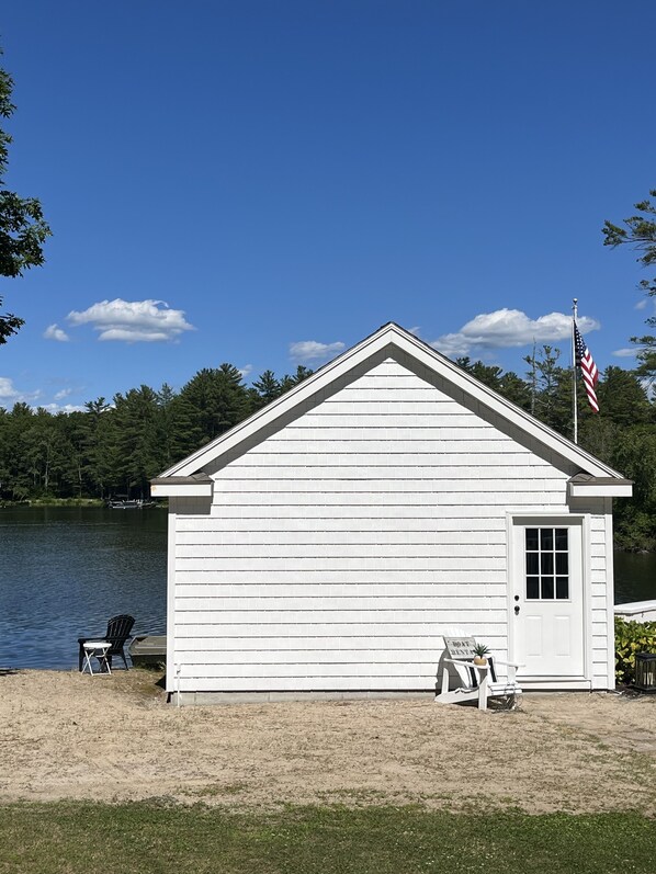 A small white building with a flag, a dock, and chairs by a lake. - NH Lakes Region Lakefront Home for rent in Wakefield NH (wakefield)