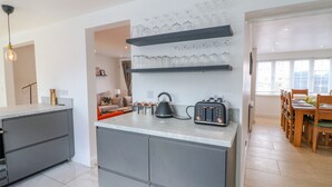 Cozinha moderna com armários cinza, bancada, torradeira e prateleira de vidro fixada na parede.