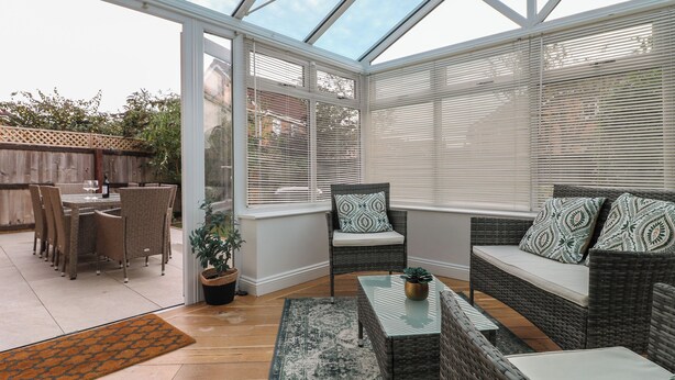 Uma estufa com móveis de vime, uma mesa de vidro e vista para o jardim.