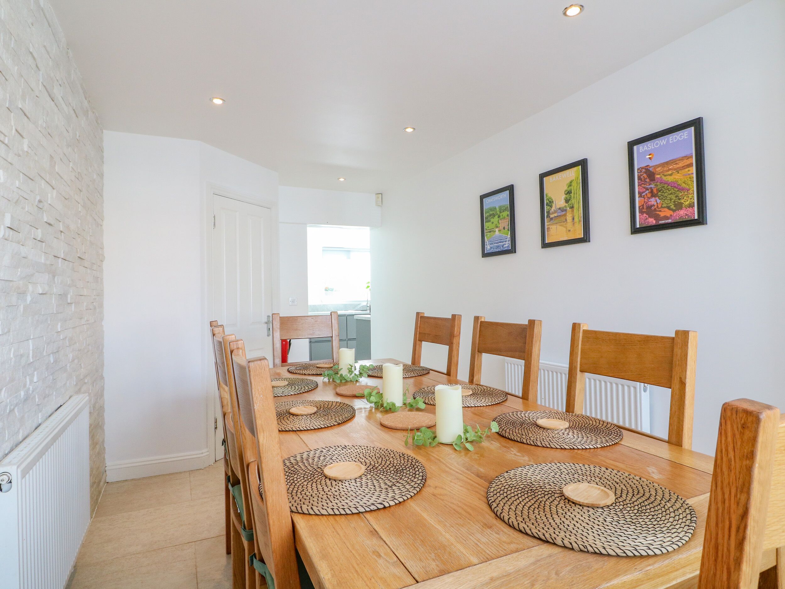 A dining area with a wooden table, six chairs, woven placemats, candles, and framed artwork on the wall.
