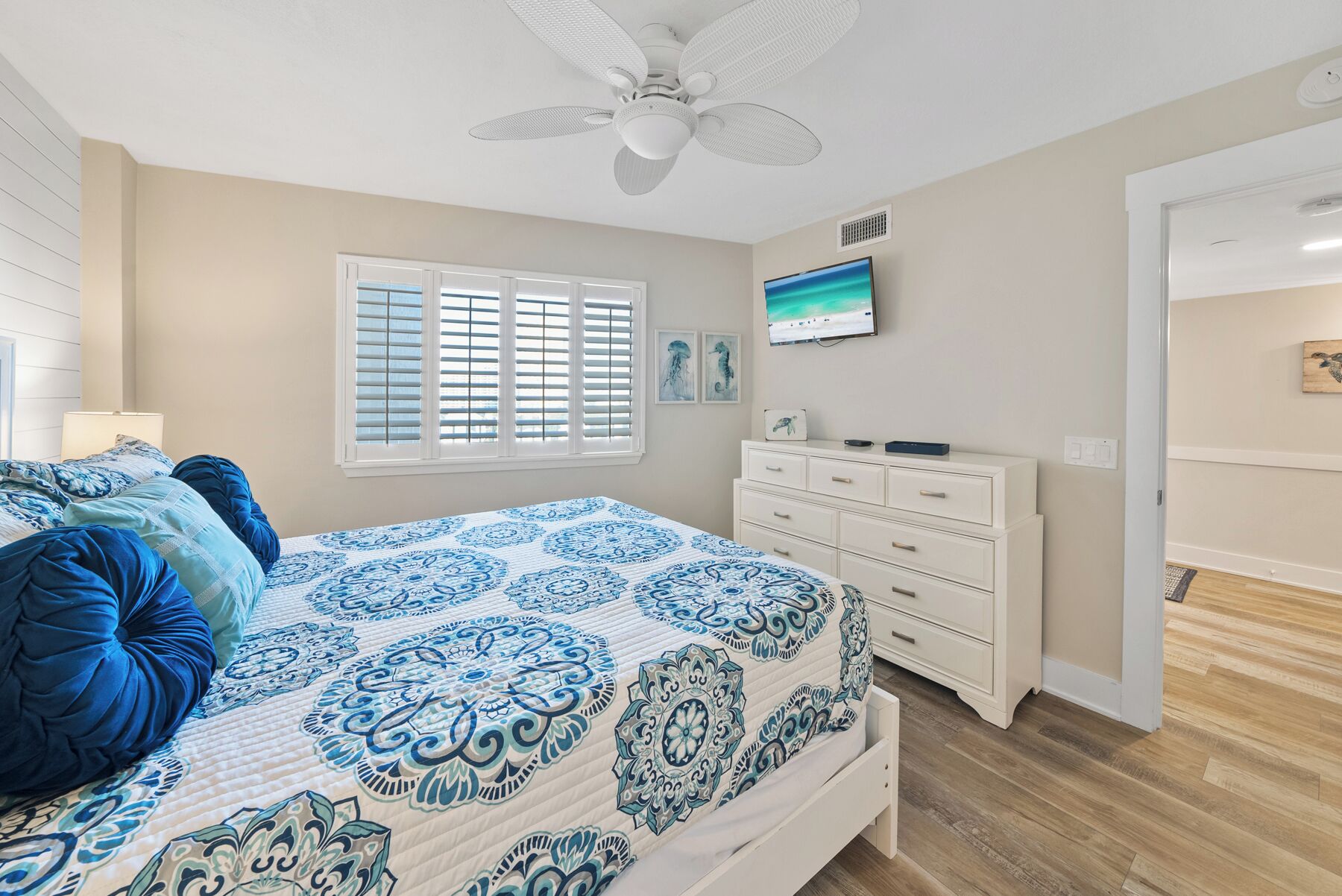 Un dormitorio con cama, televisor, cómoda y ventilador de techo.