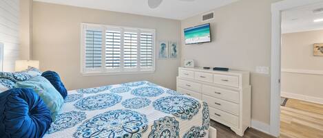 Un dormitorio con cama, televisor, cómoda y ventilador de techo.