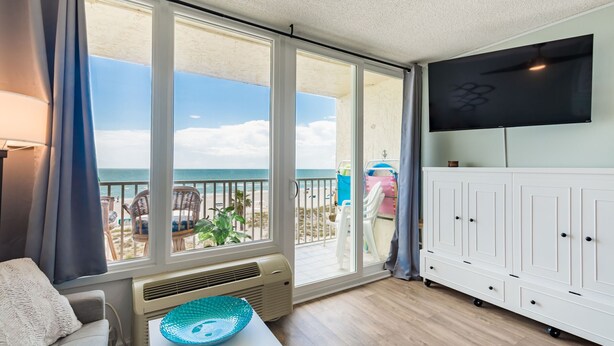 A room with a large sliding glass door leading to a balcony with a view of the beach. - Treasure Island Oceanfront Studio with Balcony & Heated Pool (Treasure Island)