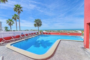 Un espace piscine avec des chaises longues, des palmiers et une vue sur l’océan.
