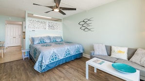 A bedroom with a bed, a ceiling fan, a white coffee table, and a gray sofa. - Treasure Island Oceanfront Studio with Balcony & Heated Pool (Treasure Island)