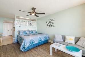 Une chambre à coucher avec un lit, un ventilateur de plafond, une table basse blanche et un canapé gris.