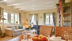 Una sala de estar acogedora con sofá, sillón y una mesa de comedor lista con comida y bebidas.