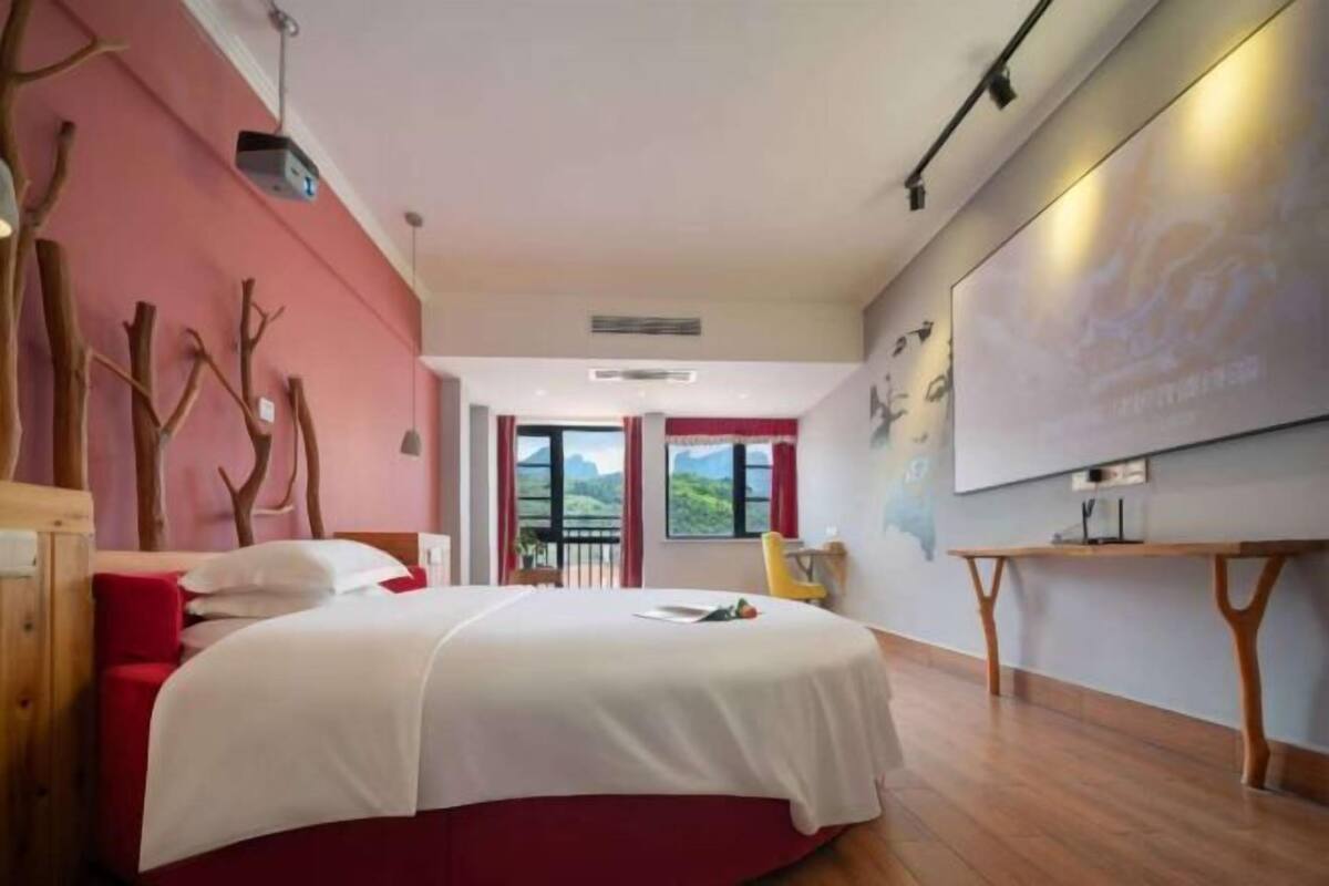 A bedroom with a bed, a desk, a chair, and a view of the outdoors.