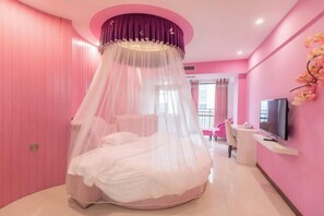 A pink-themed bedroom with a round bed, a TV, and a desk. - JIAN GE SHI GUANG TRAVEL HOTEL(Zhangjiajie Tianmenshan Cableway Station) (Zhangjiajie)