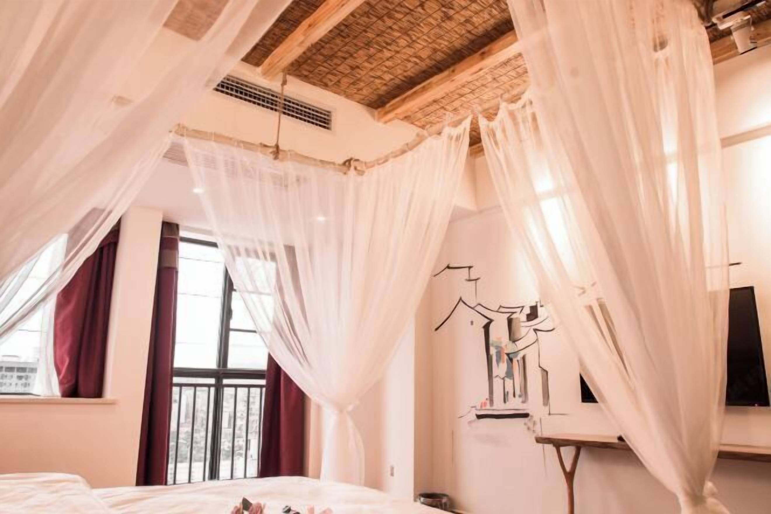 Ein Schlafzimmer mit Baldachinbett, großem Fenster und an der Wand montiertem Fernseher.