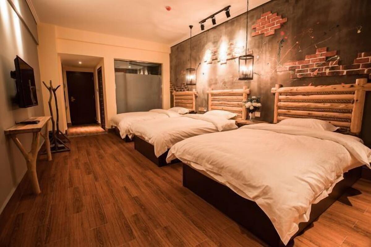 A hotel room with two beds, wooden flooring, a brick accent wall, and a TV on the left.