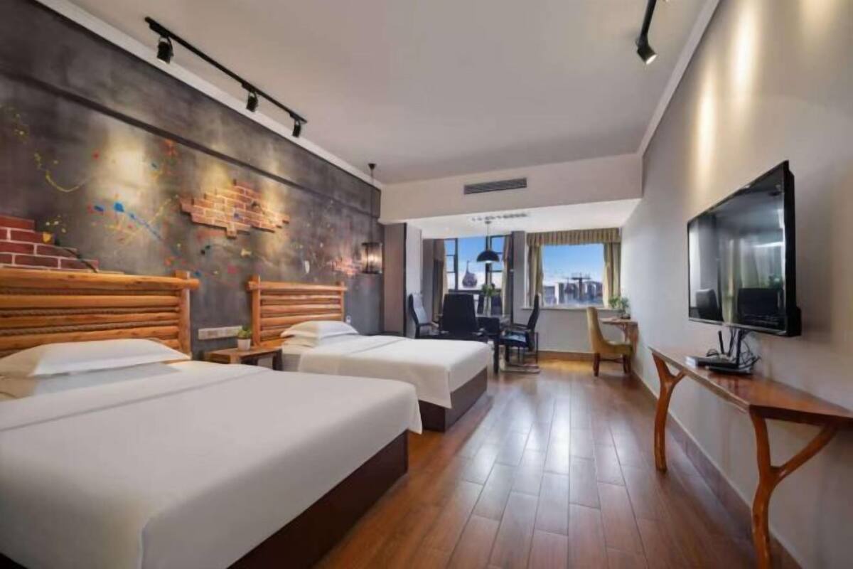 A hotel room with two beds, a desk, a TV, and a view of the city.