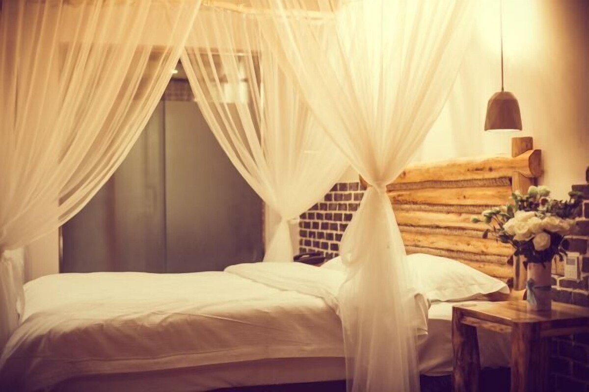 Una cama con sábanas blancas, cabecera de madera y mesita de noche con un florero.