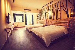 Habitación de hotel con dos camas, un escritorio y una silla. Cuenta con un ventanal con cortinas, un televisor de pared y un decorativo árbol en la pared.