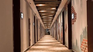 A long hallway with a patterned floor, wooden ceiling beams, and doors on both sides.